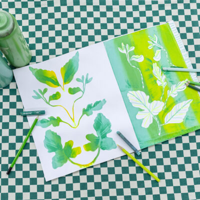 A photograph of a screenprint on paper in various shades of green. Around the print are two bottles of green ink and several drawing tools all in shades of green.