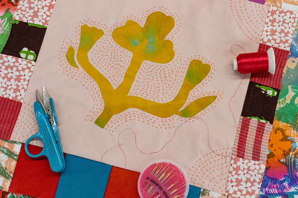 A bold, illustrative silhouette of a flower screenprinted on a quilt square with repeated lines of stitching radiating and moving outward from the printed motif.