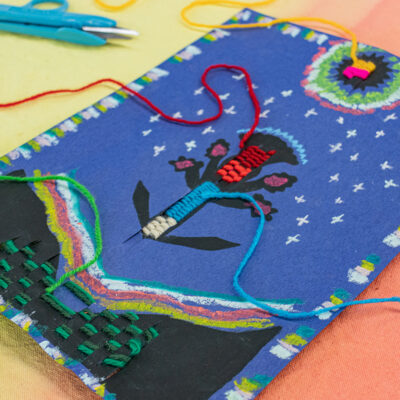 A symmetrical composition of a floral symbol under a lunar halo. The flower is being embellished with woven yarn.