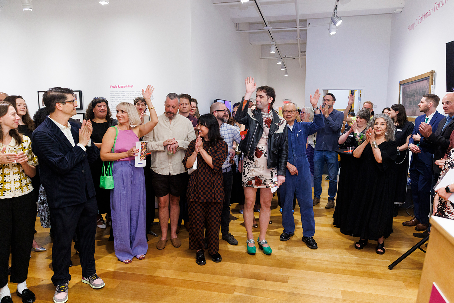 A well dressed crowd applauds while a few people raise their hands to identify themselves as artists.