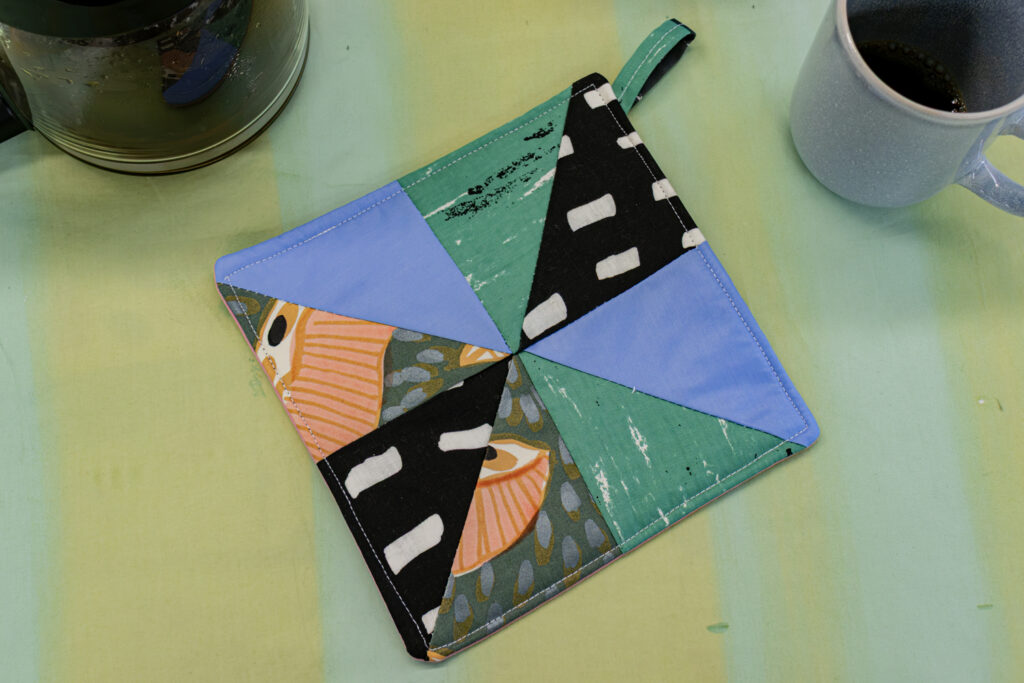 A square potholder sewn using different triangles of patterned fabrics.