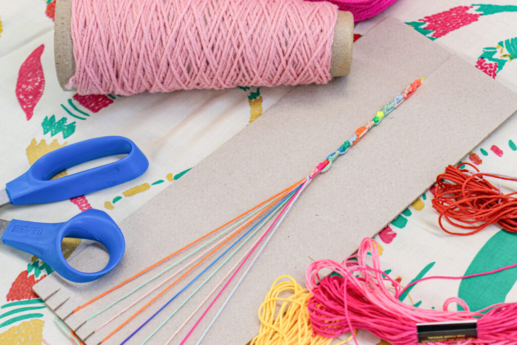 A photo of a friendship bracelet in progress. The bracelet is secured on cardstock paper as an on-the-go workspace.