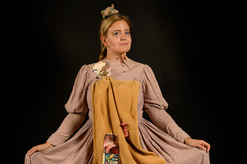 A woman stretches out her dress as if to curtsey. She is wearing plain materials in dull colors.